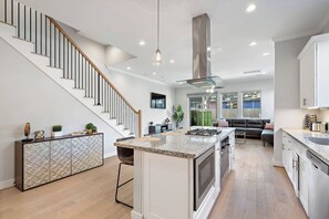 A modern kitchen with a central island, a staircase, and a dining area with a sofa.