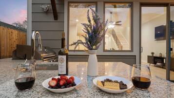 An outdoor dining area with a granite countertop, two wine glasses, a bottle of wine, and a bowl of fruit.