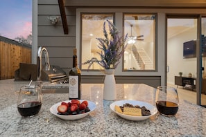 An outdoor dining area with a granite countertop, two wine glasses, a bottle of wine, and a bowl of fruit.