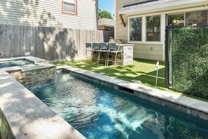 A backyard with a swimming pool, a patio with outdoor furniture, and a green lawn.