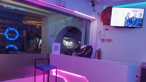 Un espace d’accueil moderne avec un comptoir éclairé par des néons, une chaise et un téléviseur fixé au mur qui diffuse une liste de lecture musicale.