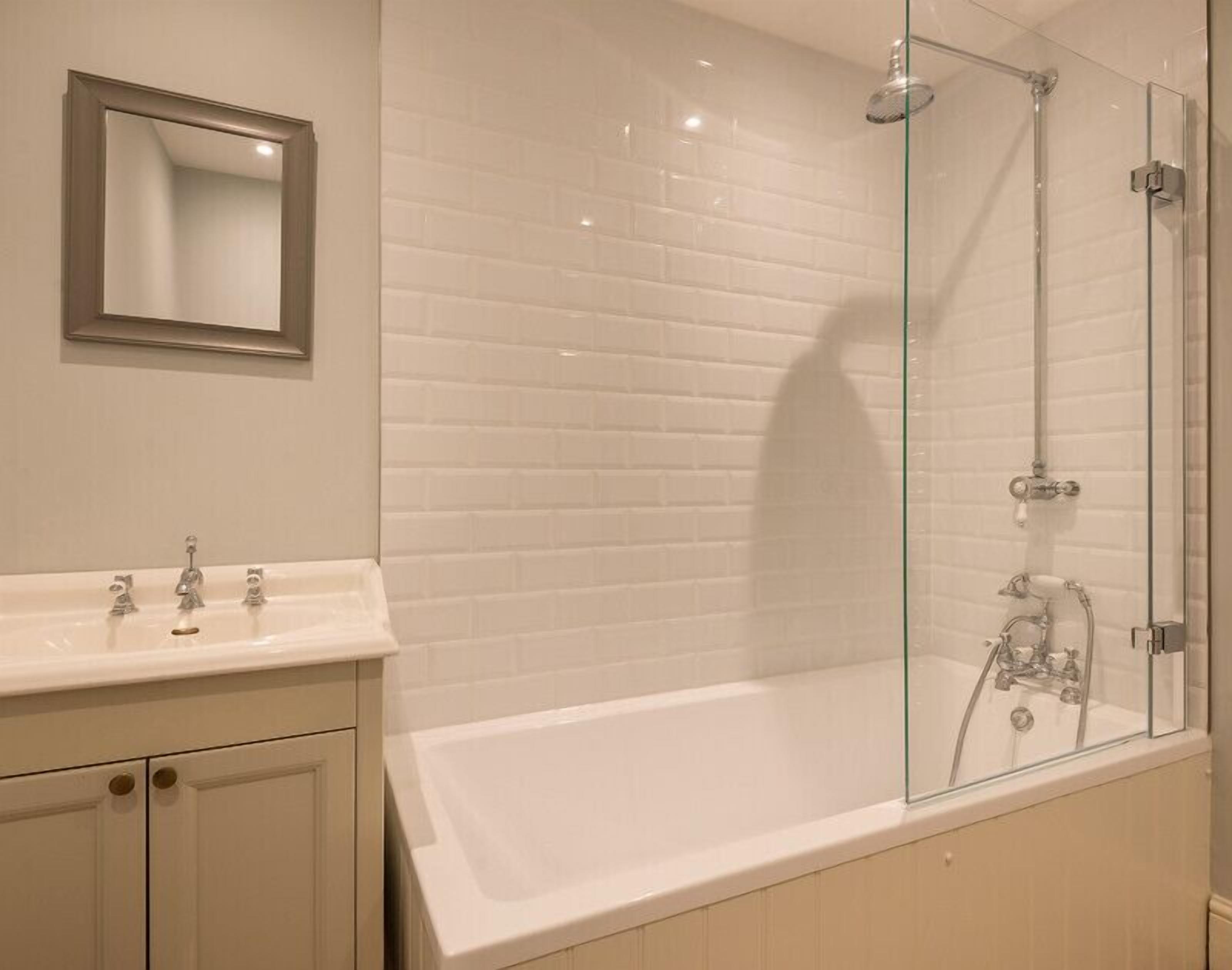 A bathroom with a white bathtub, a glass-enclosed shower, and a mirror above the sink.