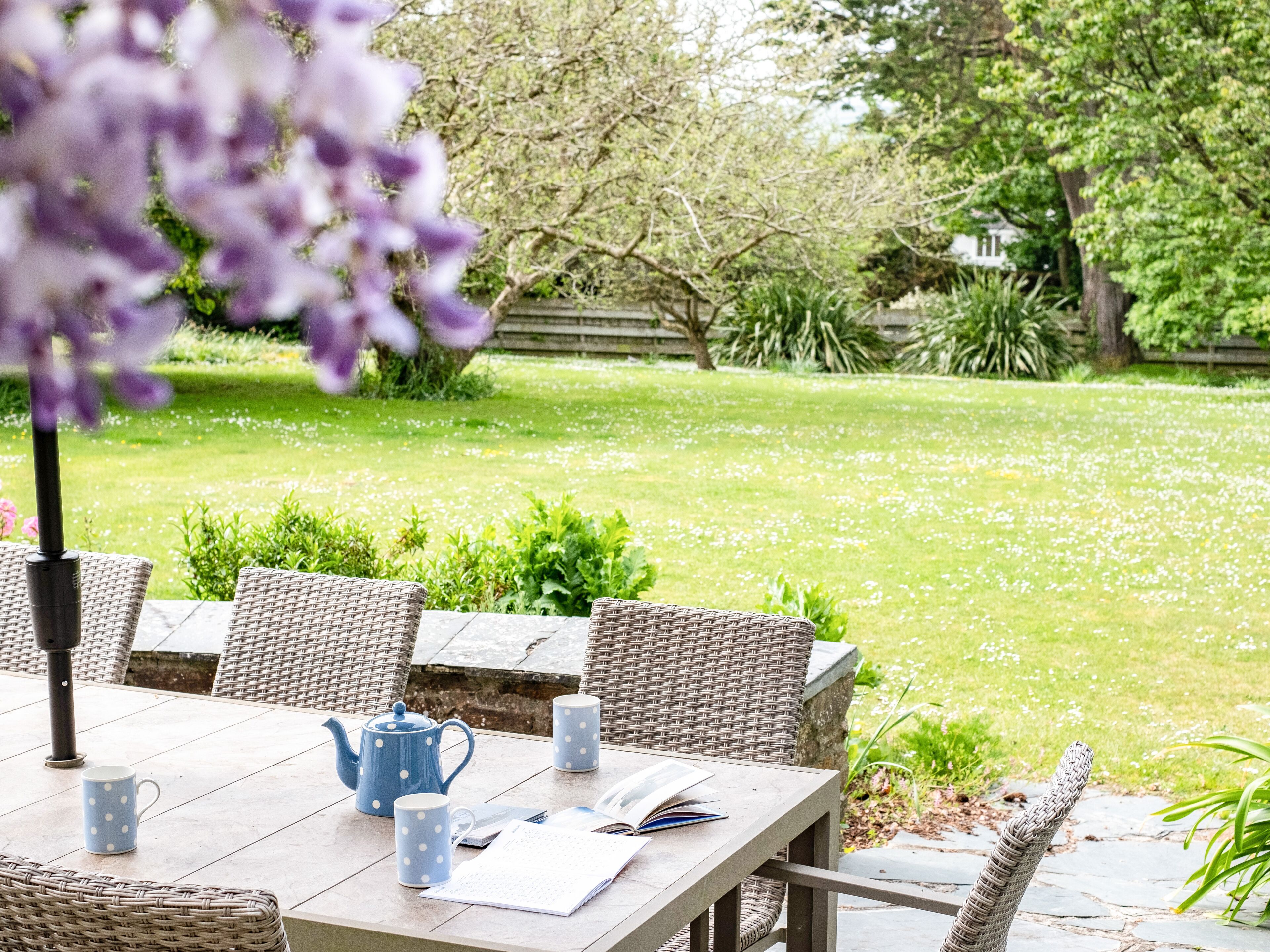 A garden patio with wicker furniture, a table, a teapot, and two mugs.