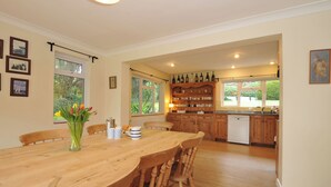 Una cocina amplia con armarios de madera, una mesa de comedor con sillas y vistas al jardín a través de ventanas grandes.