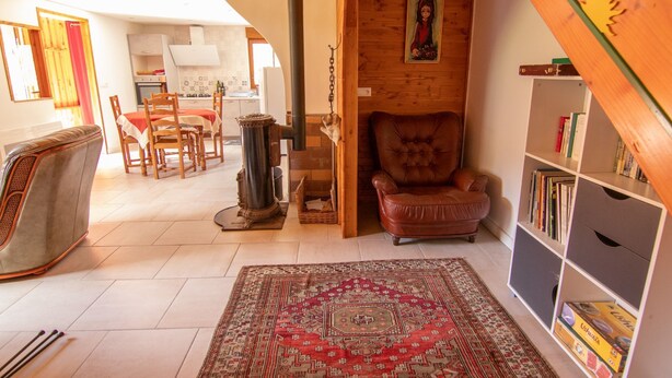 A cozy living room with a fireplace, a red armchair, a bookshelf, and a dining area with a table and chairs. - Gîte in Donezan (Quérigut)