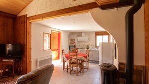 A cozy living room with a fireplace, a television, and a dining area with a red tablecloth. - Gîte in Donezan (Quérigut)