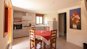 A compact kitchen with a dining area, featuring a central island, wooden chairs, and a red tablecloth. - Gîte in Donezan (Quérigut)