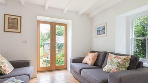 Un salon avec deux canapés gris, un parquet, une grande fenêtre et une porte donnant sur un jardin.