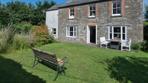 Une maison en pierre avec une cour verdoyante, un banc et une table entourée de chaises.