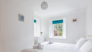 Une chambre à coucher comprenant un lit, une commode, une fenêtre donnant sur un paysage verdoyant et un luminaire suspendu.