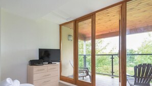 Une chambre avec un lit, une télévision, une commode et un balcon équipé de chaises.