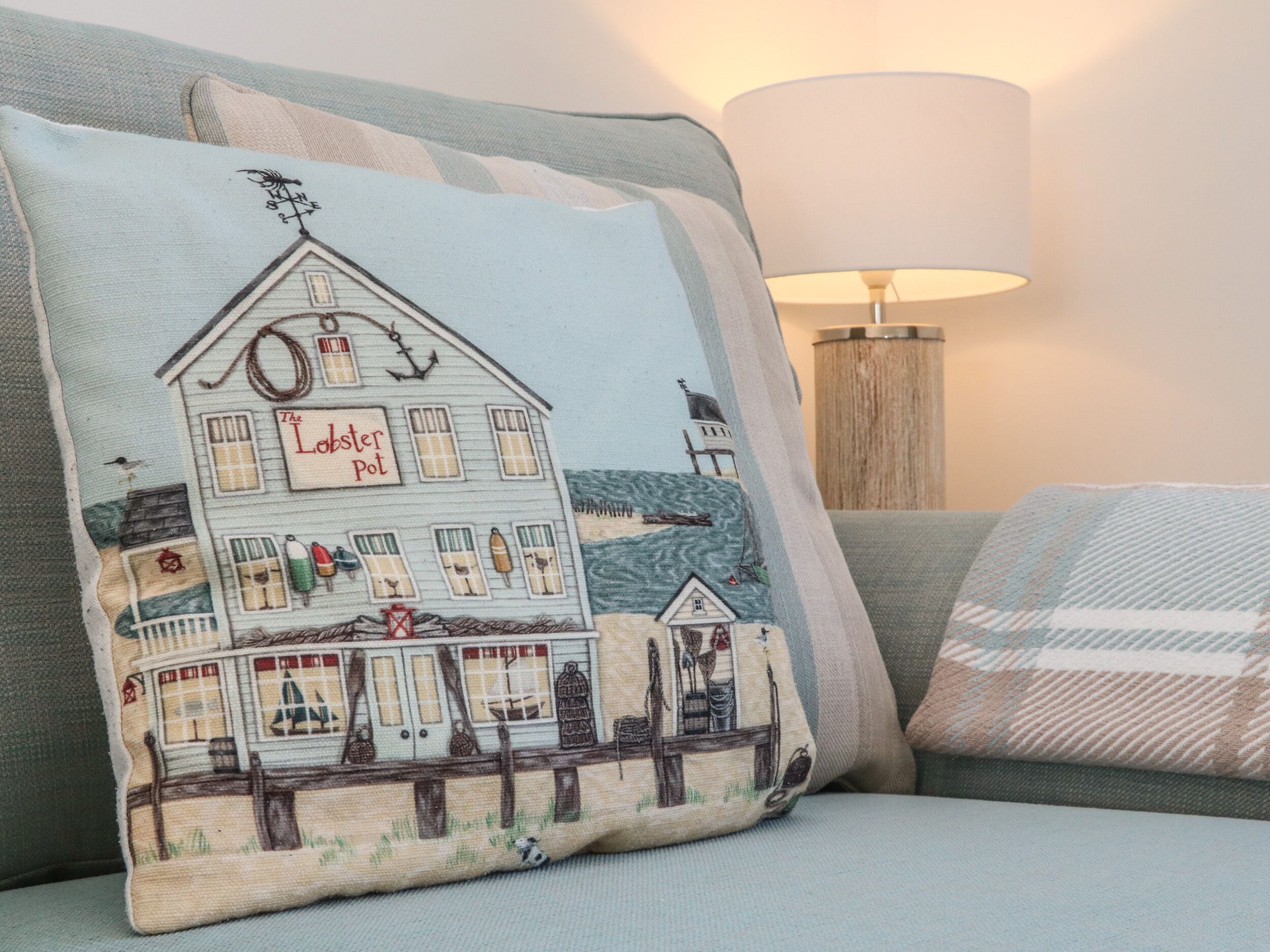 Un salon chaleureux avec un canapé et un coussin décoratif orné d’une illustration représentant un phare.