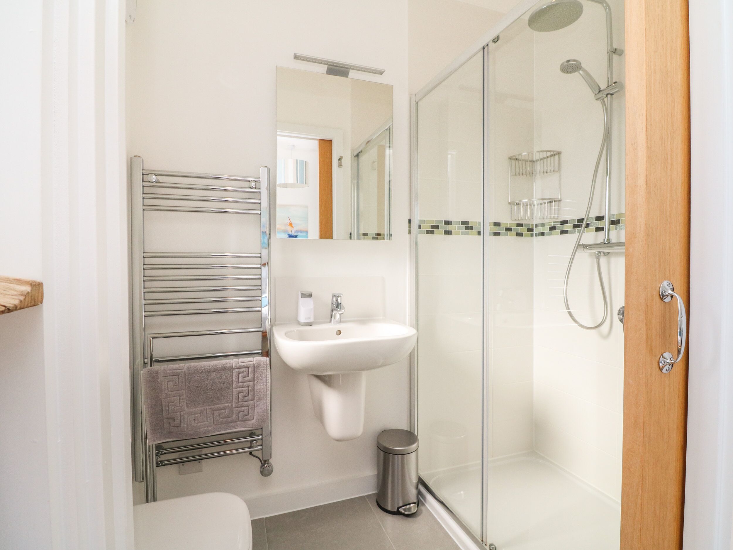 A modern bathroom with a glass shower enclosure, a white sink, and a towel rack with patterned towels.