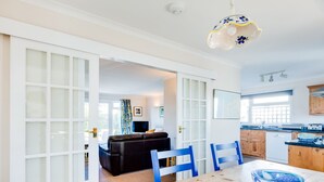 A modern kitchen with wooden cabinets, a dining table, and a blue and white bowl. - Little Sailing (Wadebridge)