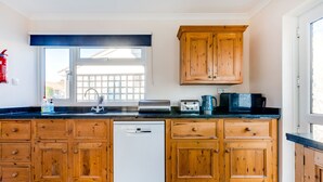 A kitchen with wooden cabinets, a dishwasher, a window, and a countertop with various appliances. - Little Sailing (Wadebridge)
