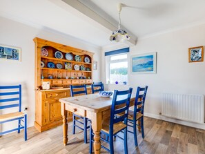 A dining area with a wooden table and chairs, a cabinet with dishes, and a window with a view. - Little Sailing (Wadebridge)