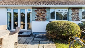 A house with a tiled roof, a brick wall, and a small garden with a hedge and outdoor furniture. - Little Sailing (Wadebridge)