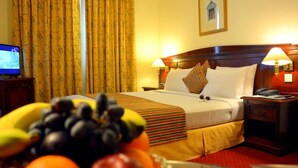 A hotel room with a bed, bedside lamps, a nightstand, a fruit bowl, and a television. - York International Hotel (Dubai)