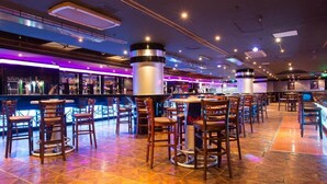 A bar area with multiple seating arrangements, including bar stools and tables, and a counter with a variety of bottles and glasses. - York International Hotel (Dubai)