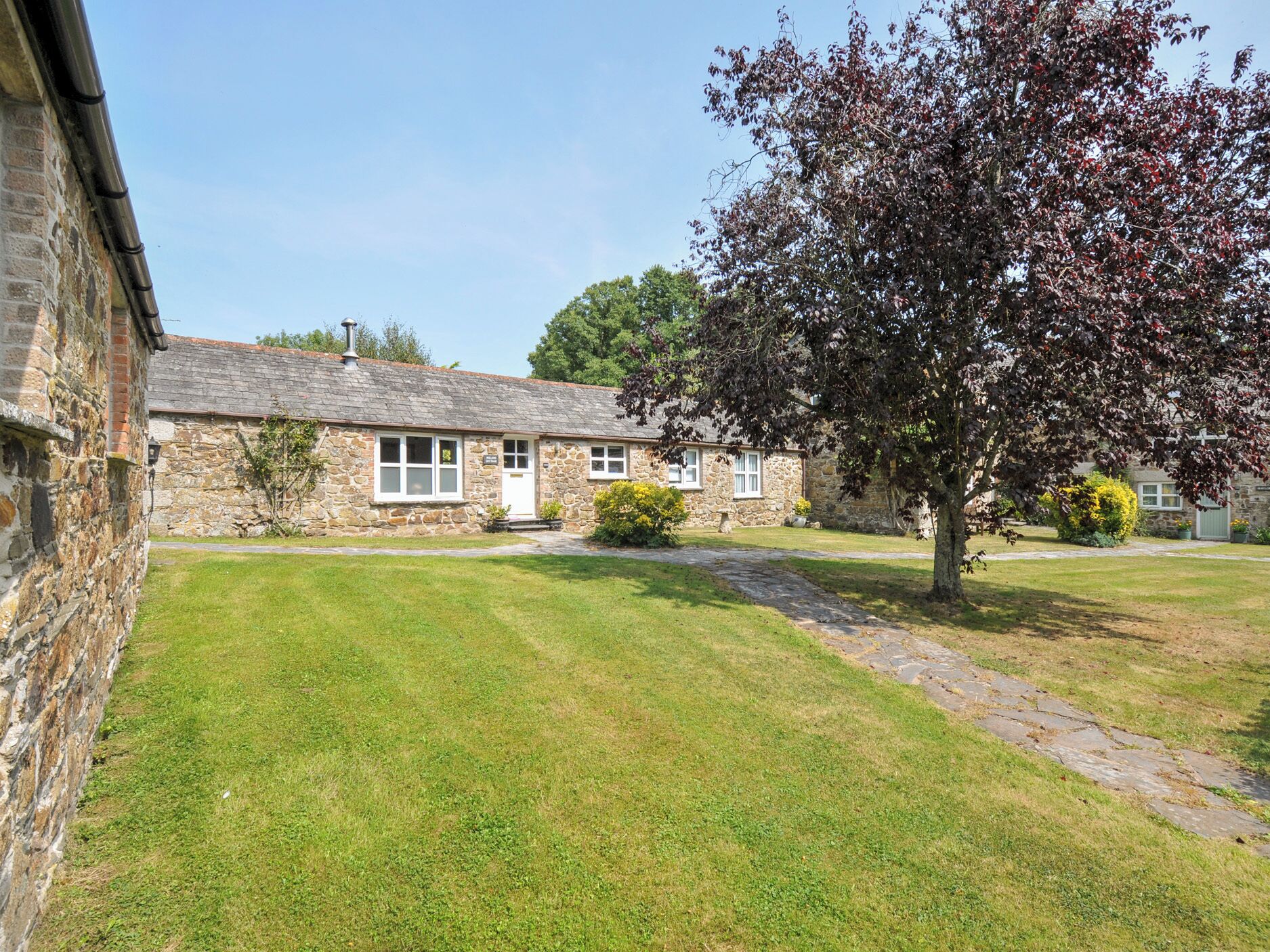 A stone cottage with a grassy yard and a tree.