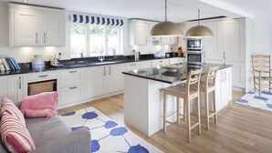 A modern kitchen with white cabinets, a black countertop, and a central island with bar stools. - Cherrytrees (Wadebridge)