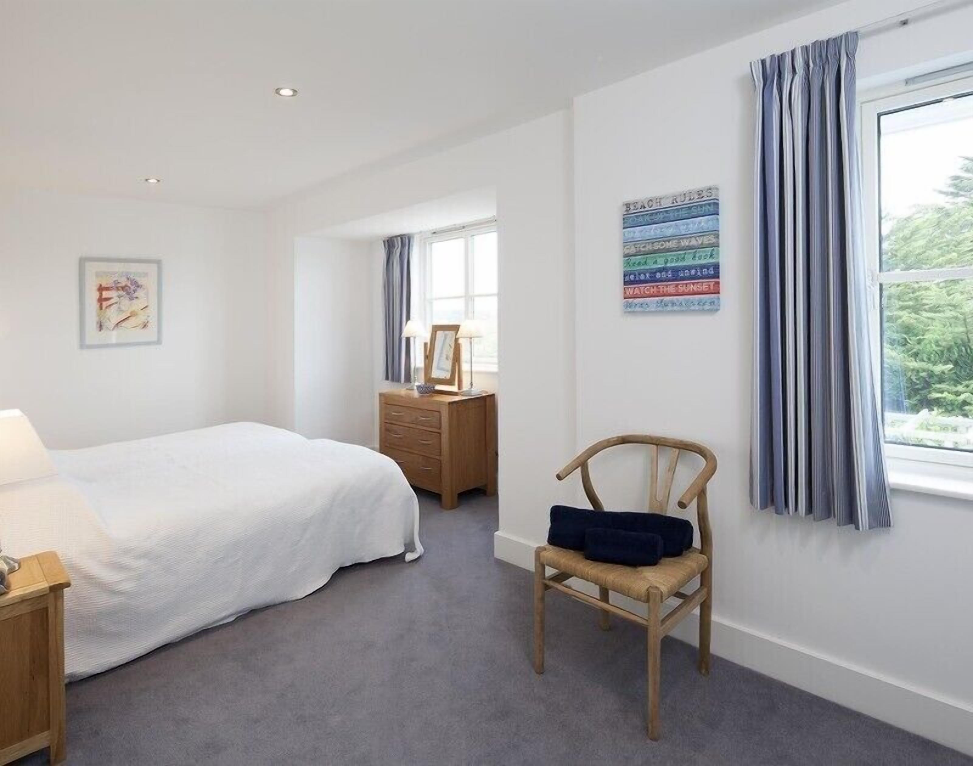 A bedroom with a bed, a wooden nightstand, a chair, a dresser, and a window with curtains.