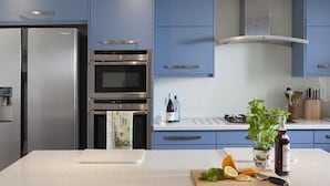 A modern kitchen with blue cabinets, stainless steel appliances, and a central island with fresh produce and a bottle of olive oil. - Downalong (Wadebridge)
