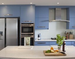 Una cocina moderna con armarios azules, electrodomésticos de acero inoxidable y una isla central con frutas frescas y una botella de aceite de oliva.