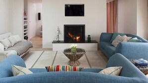 A modern living room with a fireplace, blue sofas, a coffee table, and a bookshelf. - Downalong (Wadebridge)
