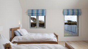 A bedroom with two single beds, a wooden bench, and two windows with striped valances. - Downalong (Wadebridge)