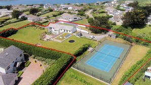 An aerial view of a residential area with houses, a tennis court, and a large building with a garden. - Downalong (Wadebridge)