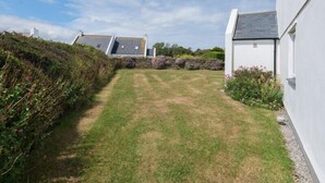 En græsplæde med en stenvæg og en hvid bygning med et gråt tag.
