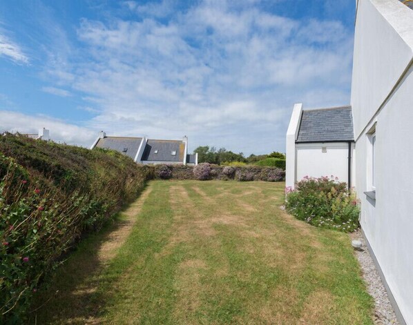 A grassy courtyard with a stone wall and a white building with a grey roof. - Kirra (Wadebridge)