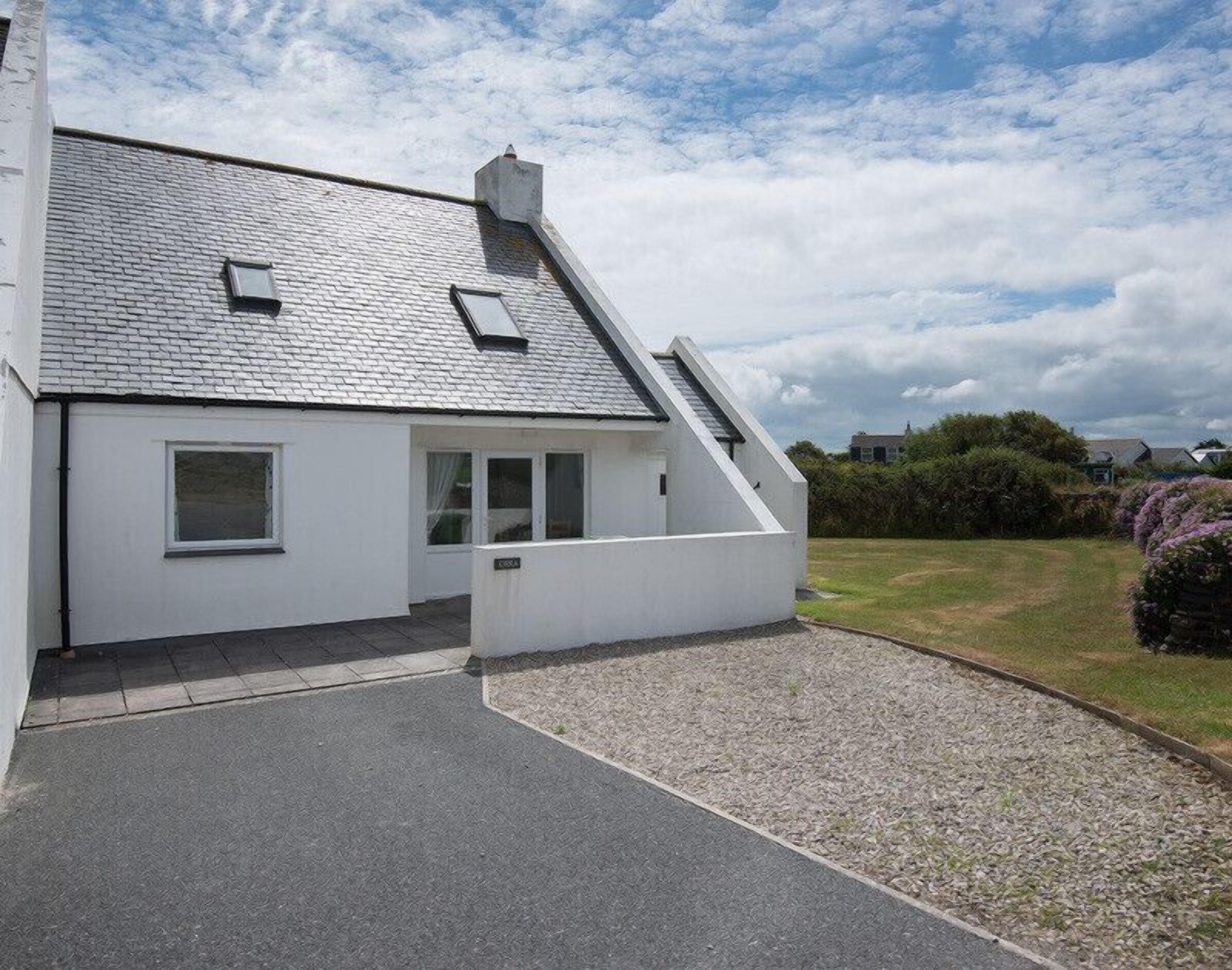 A modern house with a sloped roof, a small porch, and a gravel driveway.