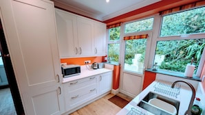 A modern kitchen with white cabinets, a microwave, a kettle, and a sink with a drying rack.
