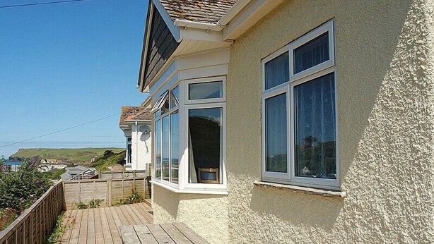 A coastal house with a wooden deck, large windows, and a view of the sea.