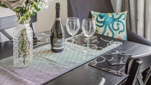 A table set with a bottle of Prosecco, two wine glasses, and a decorative vase with flowers. - Lovely Apartment Sleeps 6 Singles in Torquay (Torquay)