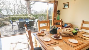 A dining area with a table set for four, a vase with flowers, and a view of the garden outside. - Old Hall Byre (Leyburn)