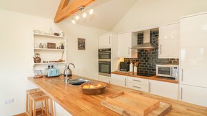 A modern kitchen with white cabinets, a wooden countertop, a sink, a toaster, and a microwave. - Old Hall Byre (Leyburn)