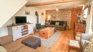 A cozy living room with a television, sofa, and a stone wall. - Old Hall Byre (Leyburn)