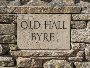 Una placa de piedra con la inscripción 'OLD HALL BYRE' colocada en una pared de piedra.