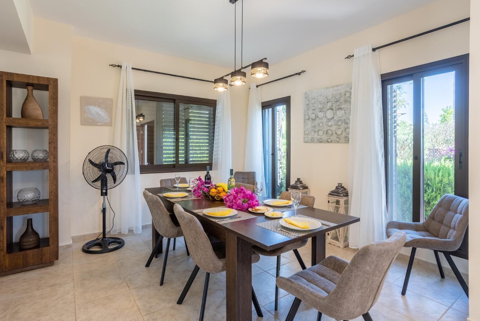 A dining area with a dark wooden table, six chairs, and a fan.