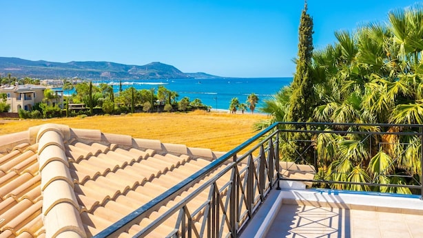 Une terrasse offrant une vue sur la mer, les palmiers et les montagnes au loin.