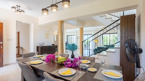 Un espace repas avec une longue table dressée pour quatre personnes, un escalier et une vue sur l’extérieur.