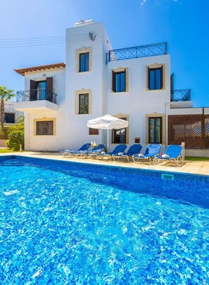 A modern building with a swimming pool, blue lounge chairs, and a white umbrella. - Villa Anna - Four Bedroom Villa, Sleeps 8 (Latchi)
