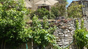 Un bâtiment en pierre, doté d’un toit en pente, entouré de verdure et d’un mur de pierre.