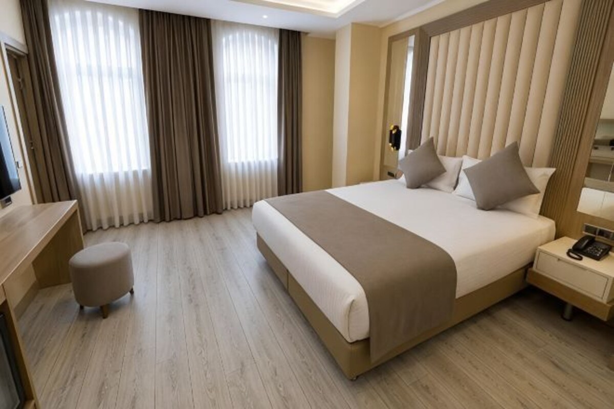 Habitación de hotel con una cama grande, un escritorio, una silla, una mesita de noche con lámpara y un teléfono.