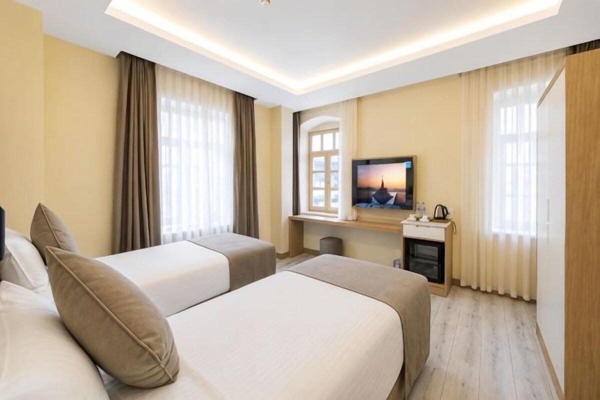 Een hotelkamer met twee bedden, een televisie, een bureau en een raam met gordijnen.