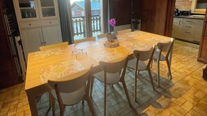 Uma sala de jantar de madeira com uma mesa grande e quatro cadeiras, um armário com portas de vidro e vista para o exterior através de uma porta deslizante.