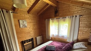 Quarto de cabana de madeira com cama, cortinas, radiador e luminária no teto.